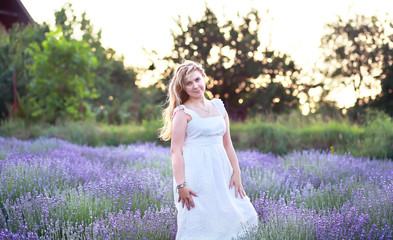 a young woman in a white sundress walks in a lavender field, enjoying the aroma and relaxing at the weekend