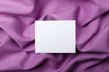 Top view of white empty card on the purple linen. Price tag or label on the fabric