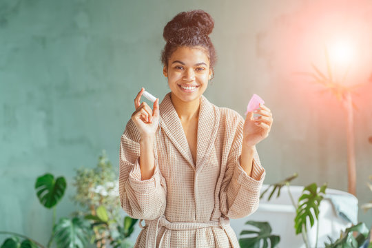 Portrait Of Positive Good Looking Black Haired Curly African Multiethnic Woman Holding Tampon And Hygiene Pad, Looking Directly At Camera, Using Tampon During Periods