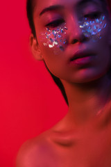 beautiful naked asian girl with rhinestones on face isolated on red, motion blur