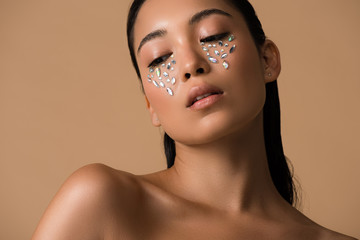 beautiful naked asian girl with rhinestones on face isolated on beige
