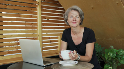 Portrait of handsome gray hair lady female looking in camera with laptop in cafe