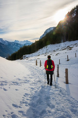 Single woman walking uphill, serene winter day in mountain, bright sun shining in the blue sky