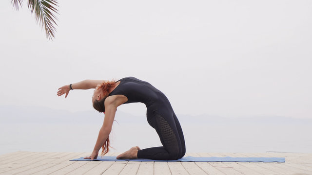 Handsome female doing hatha yoga asana at sea on foggy sunrise