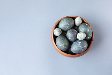 Creatively painted chicken and quail Easter eggs with natural hibiscus dye, look like sea stones in bowl on gray background, copy space. Happy Easter DIY concept. Soft selective focus. Flat lay