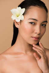 Fototapeta na wymiar beautiful naked asian girl with white lily in hair isolated on beige