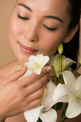 smiling beautiful naked asian girl with closed eyes and white lilies isolated on beige