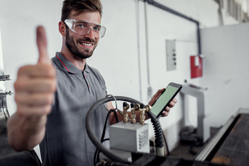 Young engineer setup plasma cutter for work in metalwork workshop, shoeing thumbs up.