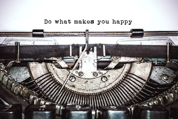 Old vintage typewriter, retro machine with white sheet of paper and typed text "do what makes you happy", copy space, close up