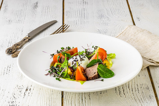 A green French bistro style salad with poached egg and chives on a white plate and table setting