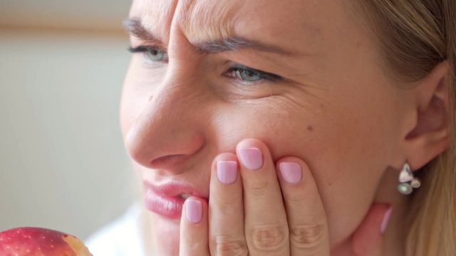 Tooth problems. Young woman having toothache, biting apple