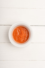 Top view of carrot puree in bowl on white wooden background