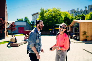Toothy male and female tourists in stylish glasses exploring city during sunny sightseeing,...