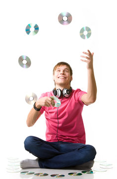 Happy young guy a music lover with headphones sits on the floor and juggles compact discs on a white background. Concept of modern and outdated music media