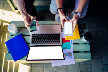 Top cropped view of millennial users connecting to bluetooth on modern palmtop devices for sharing media files during remote collaboration,laptop computer with copy space area for internet advertising