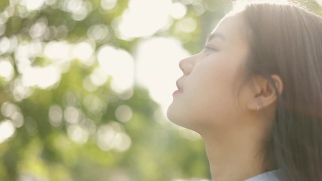 Close up portrait of young asian woman relaxed enjoying peaceful sunset and looking up exhaling fresh air relaxing at a public park on the beautiful summer sunset.