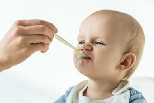 Mother feeding adorable baby with puree on white background