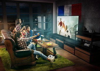 Group of friends watching TV, match, championship, sport games. Emotional men and women cheering for favourite football team of France with flag. Concept of friendship, sport, competition, emotions.