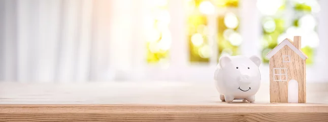 Fotobehang Piggy bank and model house on a bright interior room background © Li Ding