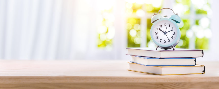 Stack of Books with Alarm Clock on Wooden Desk