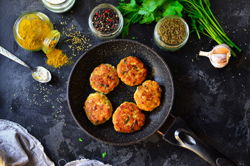 Meatballs in a pan. Chicken cutlets in a pan on a dark concrete table background. Top view. Ingredients and cooked meatballs. Spices, parsley, meat dish.