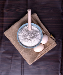 A bowl of flour with eggs on tablecloth