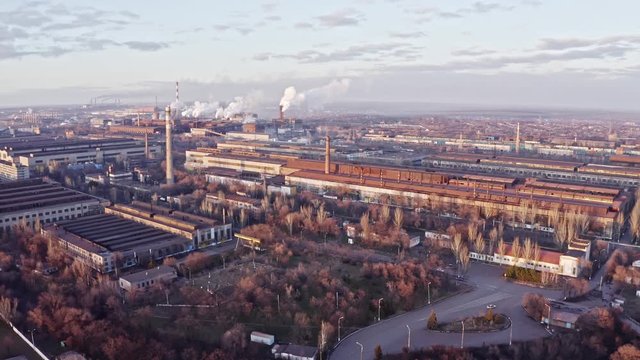 Aerial view. Emission to atmosphere from industrial pipes metallurgic factory. Smokestack pipes at plant shoot with drone. Aerial drone footage of steel factory pipes during sunrise time.