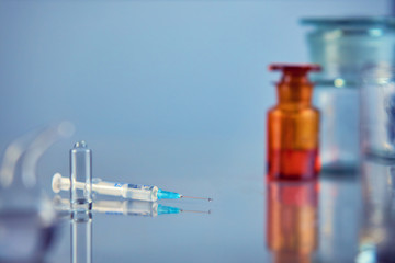 A medical ampoule with a syringe lies on a mirror table, on a blue background
