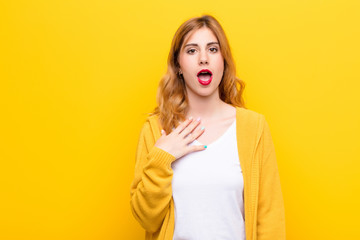 young pretty blonde woman feeling shocked, astonished and surprised, with hand on chest and open...