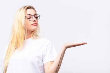 young pretty blonde woman feeling happy and smiling casually, looking to an object or concept held...
