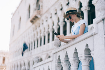 Happy tourist in straw hat reading network news during summer vacations in Italy, smiling female...