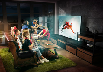 Group of friends watching TV, match, championship, sport games. Emotional men and women cheering for favourite snowboarder, look on fighting for ball. Concept of friendship, competition, emotions.