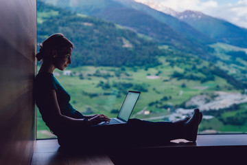 Skilled female digital nomad working remotely creating trip guide to high mountains for share to followers in social networks connected to 4g internet, skilled freelancer typing text on laptop