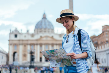 Fototapeta premium Attractive Caucasian tourist checking information from paper map for navigate own location during city sightseeing in ancient Rome,beautiful female traveller exploring Vatican city during Italian trip