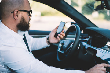 Businessman reading received smartphone notification while using self-driving in contemporary car...