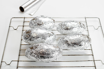 Large raw potatoes for cooking wrapped in foil and lie on the oven racks on a white table