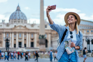 Cheerful woman in joyful mood holding navigation map and clicking cellphone images via medial...