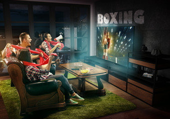 Fototapeta premium Group of friends watching TV, boxing match, championship, sport games. Emotional men and women cheering for favourite boxer, look on fighting. Concept of friendship, sport, competition, emotions.
