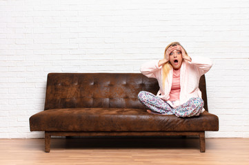 young pretty blonde woman feeling horrified and shocked, raising hands to head and panicking at a...