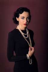 Portrait of a girl in the style of the golden 20s. Young woman in a black dress and a pearl beads....