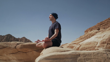 Fototapeta na wymiar Handsome male sitting in lotus pose on a rock in desert