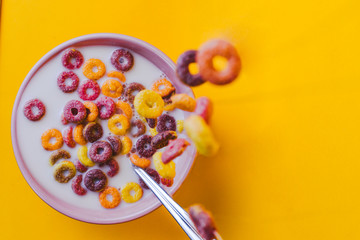 Colored cereals falling in a pink bowl with milk and a spoon.
