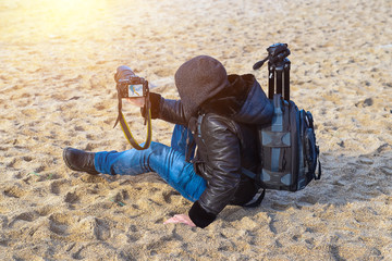 Photographer traveler with a camera and a backpack on the beach in spring when it is still cold, takes pictures