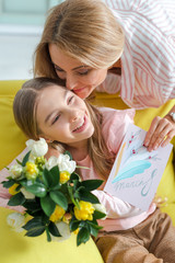 happy mother holding greeting card with 8 march lettering while kissing daughter at home
