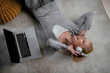 Beautiful woman lying on floor listening music . Top view of woman singing and having fun at home. 
