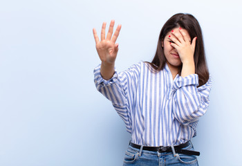 young pretty woman covering face with hand and putting other hand up front to stop camera, refusing...
