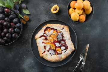 Tasty fall pie galette with plum and apricot on black table.