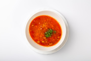 Beef goulash soup with tongue. A white oval plate with red soup stands on a white background. The view from the top