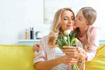 Fototapeta na wymiar cute daughter kissing happy mother holding bouquet of tulips