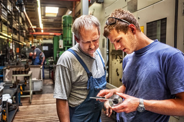 Skilled workers standing in a production hall in front of a machine tool, checking a workpiece